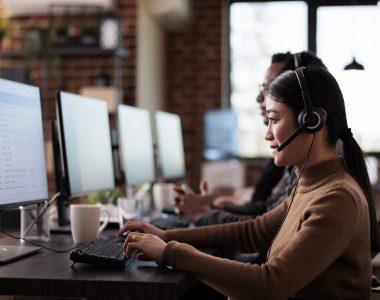 Paralyzed asian employee working at call center reception in disability friendly office. Female operator wheelchair user with impairment giving assistance on customer service helpline.